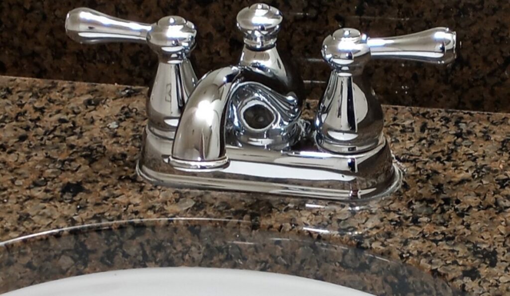 A polished chrome bathroom faucet and clean granite countertop, showcasing detailed cleaning by By Grace Cleaning Solutions, LLC in Cincinnati, OH.