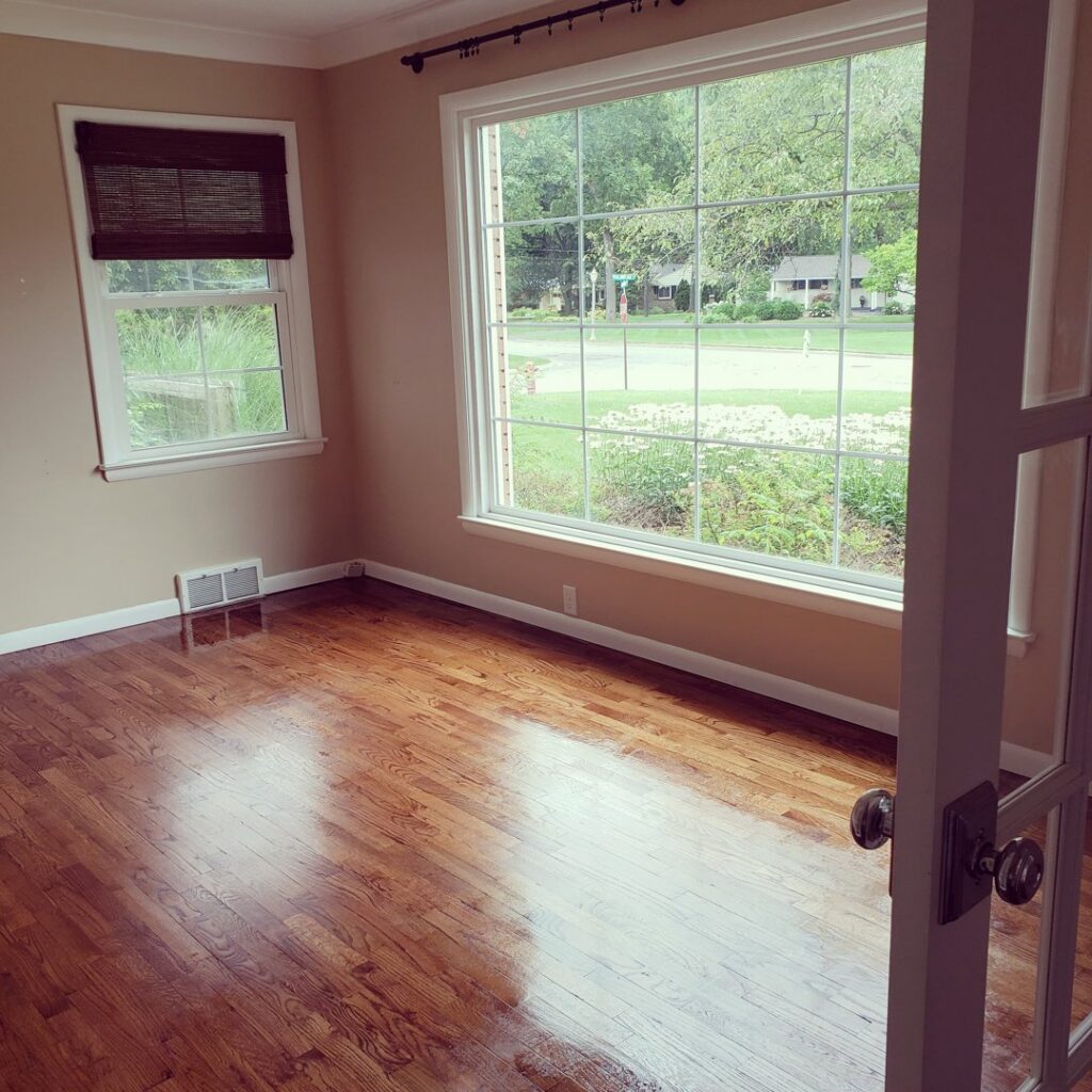 A room with beautifully polished hardwood floors and a large window, professionally cleaned by A To Zen in Lansing, MI.