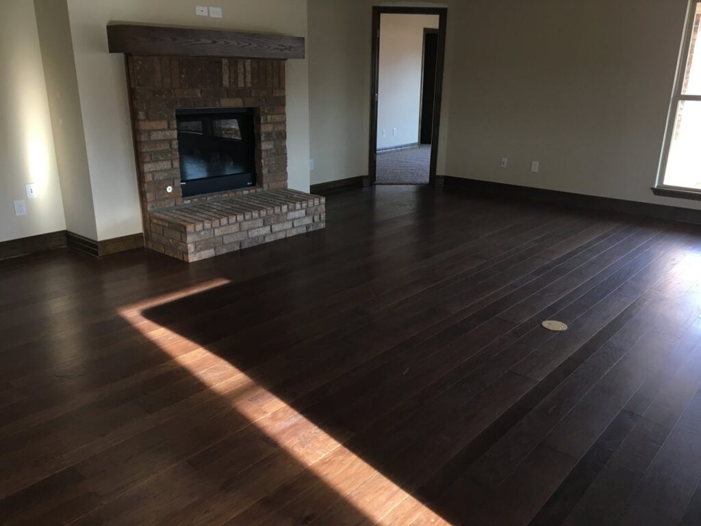Gleaming, polished hardwood floors in a living room with a brick fireplace, cleaned by Pristine Cleaning Concepts in Stillwater, OK.