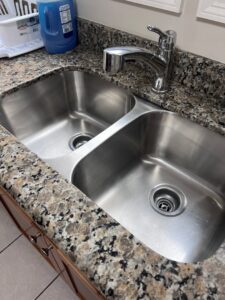 A polished double-basin kitchen sink with a gleaming granite countertop, expertly cleaned by JBO Cleaning Services in Belle Chasse, LA.