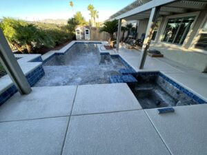 A pool and spa under renovation, drained with exposed concrete surfaces and blue tiles, by Fix A Pool in Las Vegas, NV
