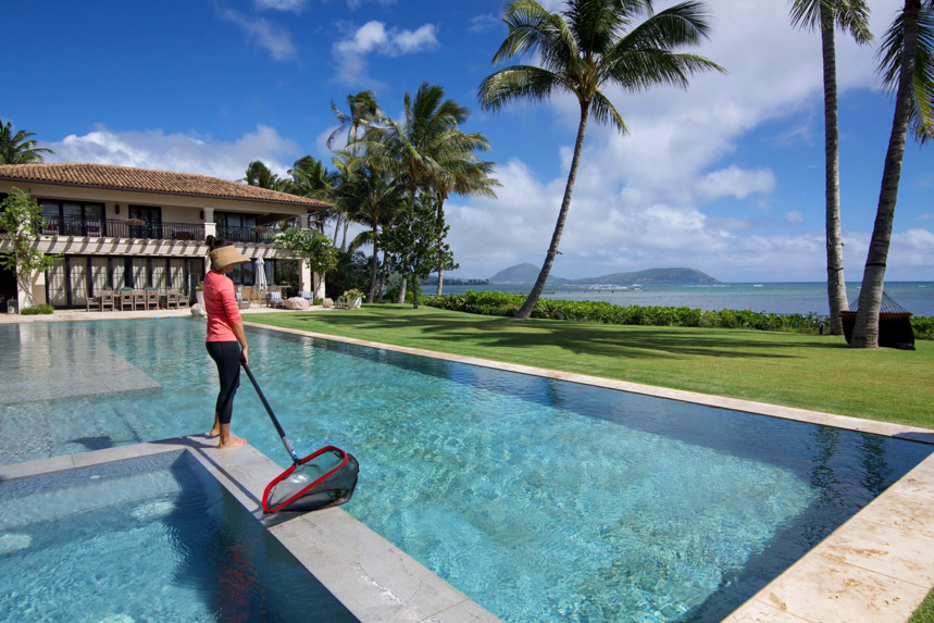 A pool cleaner skimming an infinity pool with a net at a beautiful property by East Oahu Pools in East Honolulu, HI.