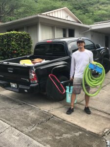 A pool cleaner standing with cleaning equipment next to a service truck for East Oahu Pools in East Honolulu, HI.