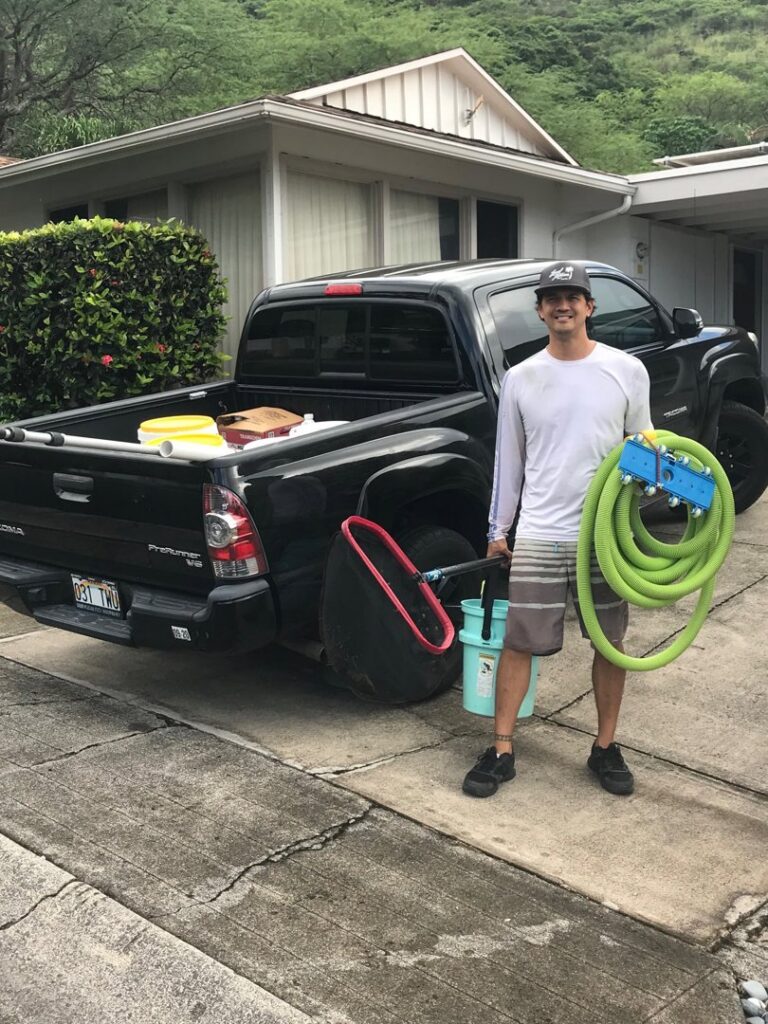 A pool cleaner standing with cleaning equipment next to a service truck for East Oahu Pools in East Honolulu, HI.