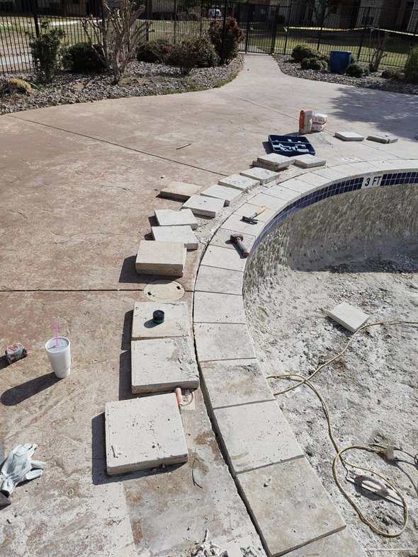 Close-up view of new coping tiles being carefully laid around the edge of an empty pool by J.R. Pools in Lubbock, TX.