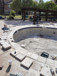 An empty pool with new coping tiles being installed around the edge by J.R. Pools in Lubbock, TX.