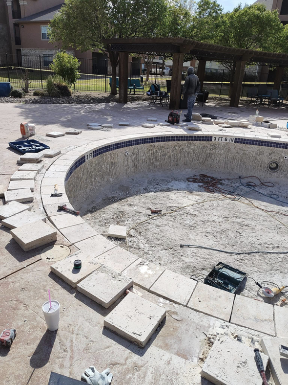 An empty pool with new coping tiles being installed around the edge by J.R. Pools in Lubbock, TX.
