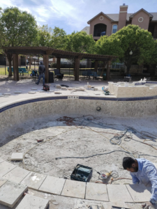 Workers installing new coping and deck tiles around an empty pool during renovation by J.R. Pools in Lubbock, TX.