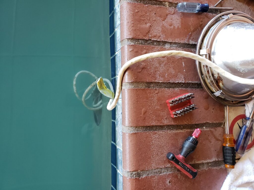A pool light fixture being repaired with tools next to a clean pool by Thompson Pools in Statesboro, GA.