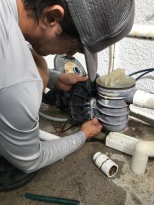 A pool technician performing maintenance or repair on a pool pump system for East Oahu Pools in East Honolulu, HI.