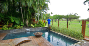 A pool service technician cleaning a small residential pool with a pole at East Oahu Pools in East Honolulu, HI.