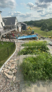 A swimming pool shell being carefully lowered into an excavated hole during installation by Backyard Escapes by Kerner Pools & Spas in Bismarck, ND.