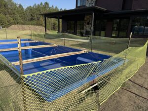 A swimming pool shell surrounded by a temporary safety fence during installation by Backyard Escapes by Kerner Pools & Spas in Bismarck, ND.