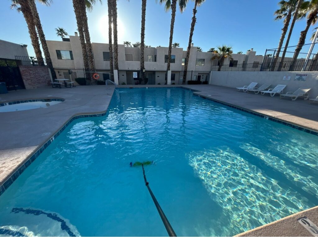 A pool technician using a skimmer net to remove debris from a residential pool by Overflow Poolz LLC in Las Vegas, NV.
