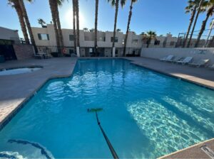 A pool technician using a skimmer net to remove debris from a residential pool by Overflow Poolz LLC in Las Vegas, NV.