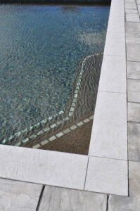 A close-up detail of pool steps with blue tiling and clean coping by Christman Pool Service in Portland, ME.