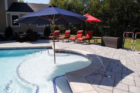A beautiful inground pool featuring a sun shelf with an umbrella, built by Christman Pool Service in Portland, ME.