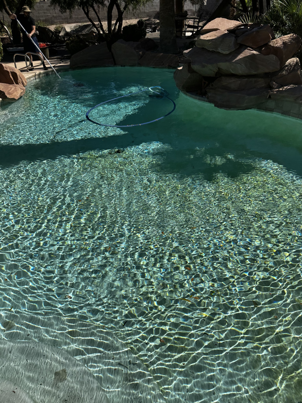 A pool technician actively cleaning a residential pool with a vacuum hose for AquaMac Pool Cleaning Service LLC in Reno, NV.