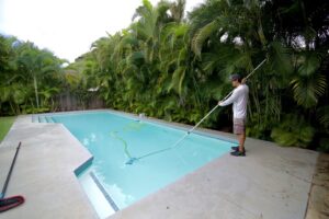 A pool technician vacuuming a residential swimming pool as part of services by East Oahu Pools in East Honolulu, HI.