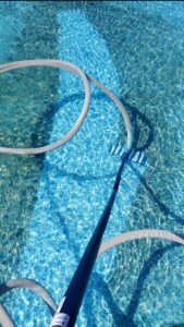 A pool vacuum and hose actively cleaning the bottom of a swimming pool by Platinum Pools in Houston, TX