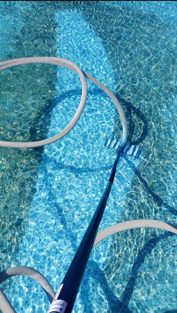 A pool vacuum and hose actively cleaning the bottom of a swimming pool by Platinum Pools in Houston, TX
