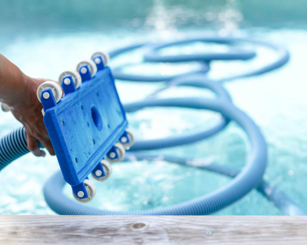 A hand holding a pool vacuum head with a hose, actively cleaning a swimming pool by HappyPools LLC in North Las Vegas, NV.