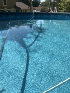 A pool vacuum hose submerged in a clean, blue above-ground pool by Pips Pool Service in Enid, OK.