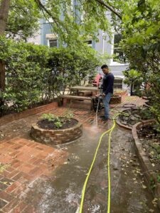 A professional pressure washing a brick patio in a backyard, a service offered by Procleanersofdmv in Rockville, MD.