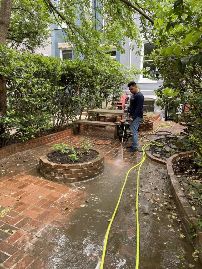 A professional pressure washing a brick patio in a backyard, a service offered by Procleanersofdmv in Rockville, MD.