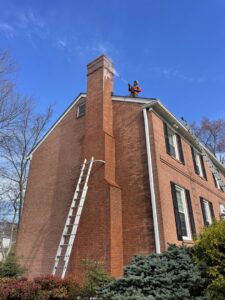 A professional pressure washing a brick house chimney from the roof, provided by Procleanersofdmv in Rockville, MD.