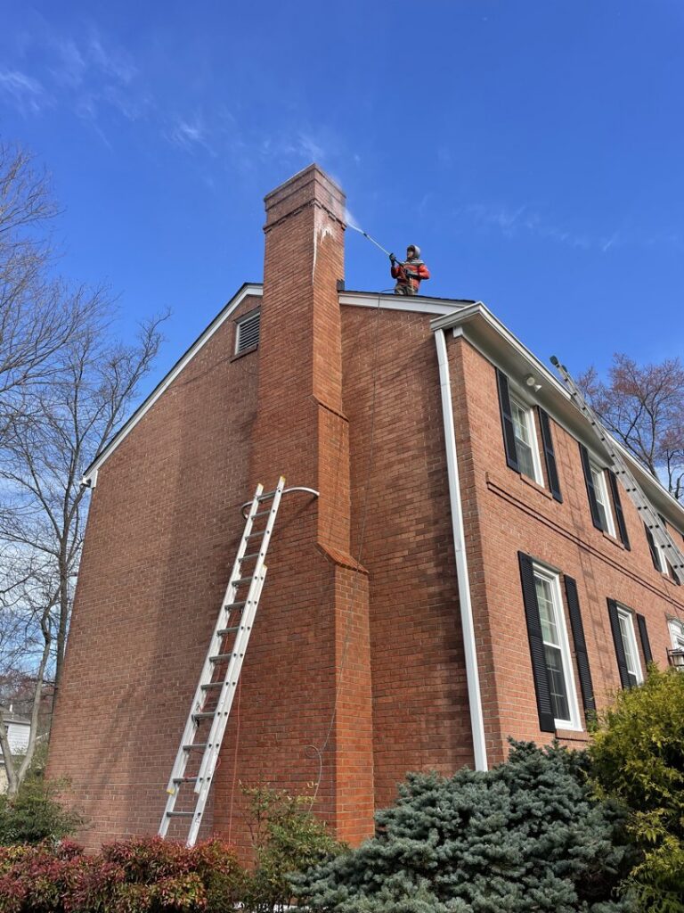 A professional pressure washing a brick house chimney from the roof, provided by Procleanersofdmv in Rockville, MD.