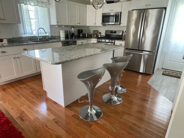 A pristine kitchen with white cabinets, granite island, and stainless steel appliances by Straight Up Cleaning in South Portland, ME.