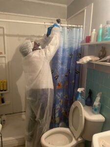A professional cleaner in protective gear sanitizing a shower head in a bathroom by Skedaddle Cleaning Services in Eufaula, AL.