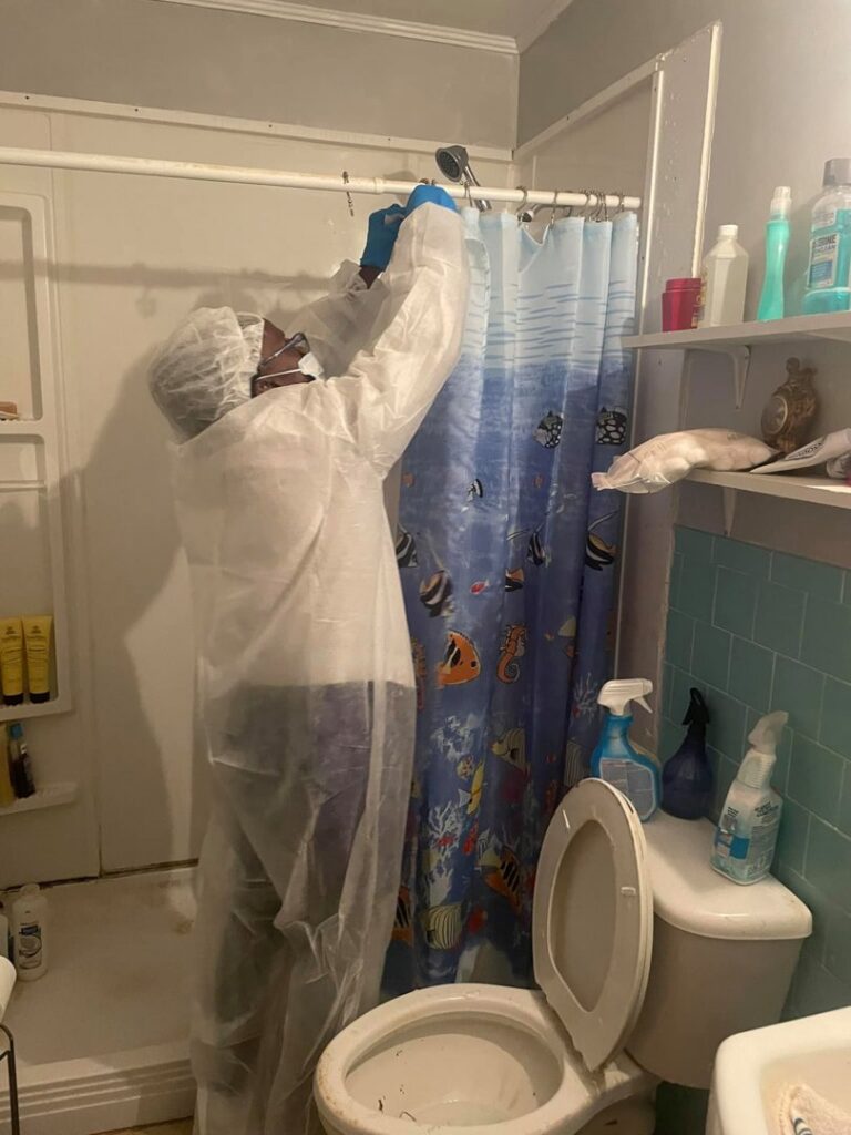 A professional cleaner in protective gear sanitizing a shower head in a bathroom by Skedaddle Cleaning Services in Eufaula, AL.