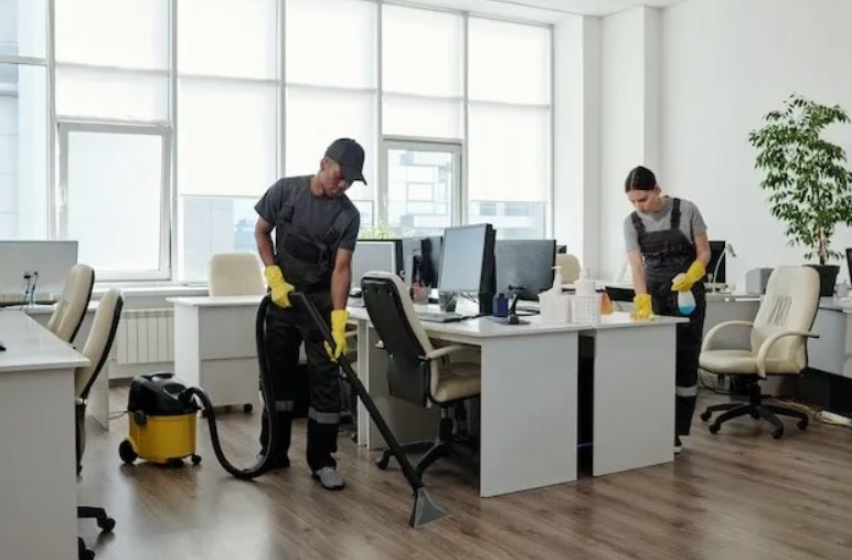 Professional cleaners vacuuming and wiping desks in an office space, provided by Stella's Professional Cleaning LLC in Wilmington, NC.