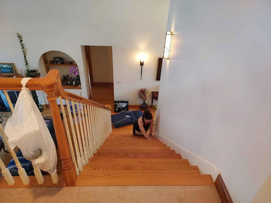 A professional house cleaner from KDG Decluttering meticulously cleaning wooden stairs in Manchester, NH.