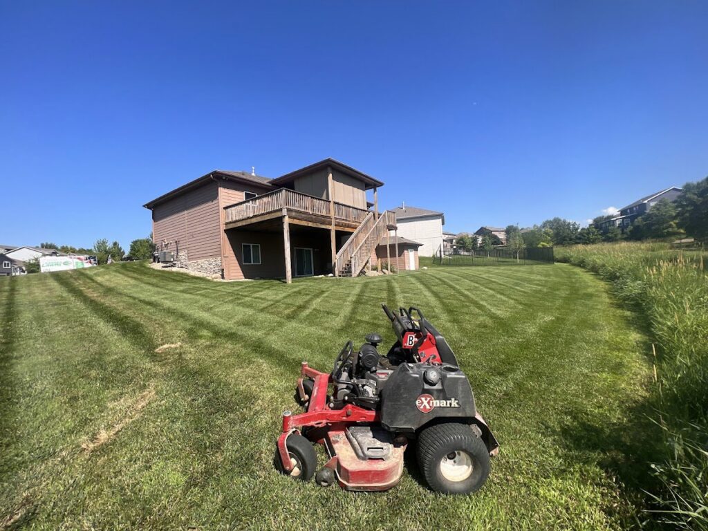 A professional zero-turn lawn mower on a large, beautifully striped lawn maintained by Kanger Lawns LLC in Omaha, NE.