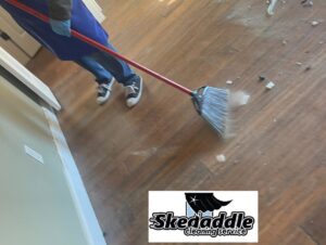 A professional cleaner sweeping a wooden floor with a broom, demonstrating floor care by Skedaddle Cleaning Services in Eufaula, AL.