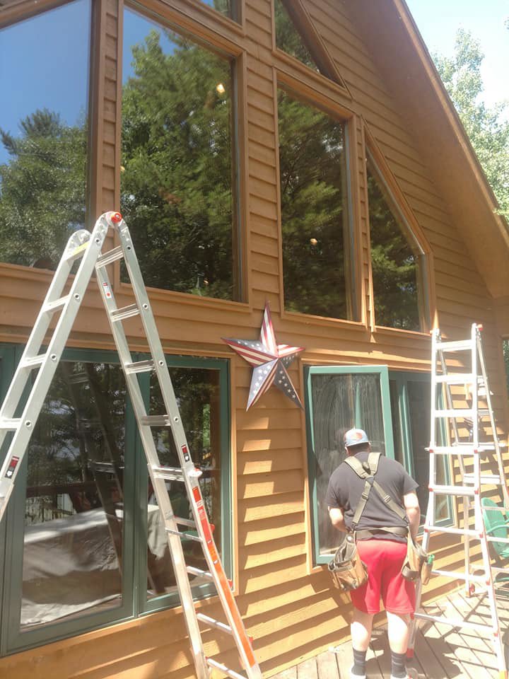 A professional cleaner on a ladder cleaning exterior windows of a house by Wholesome-Green Cleaning in Saint Croix Falls, WI.