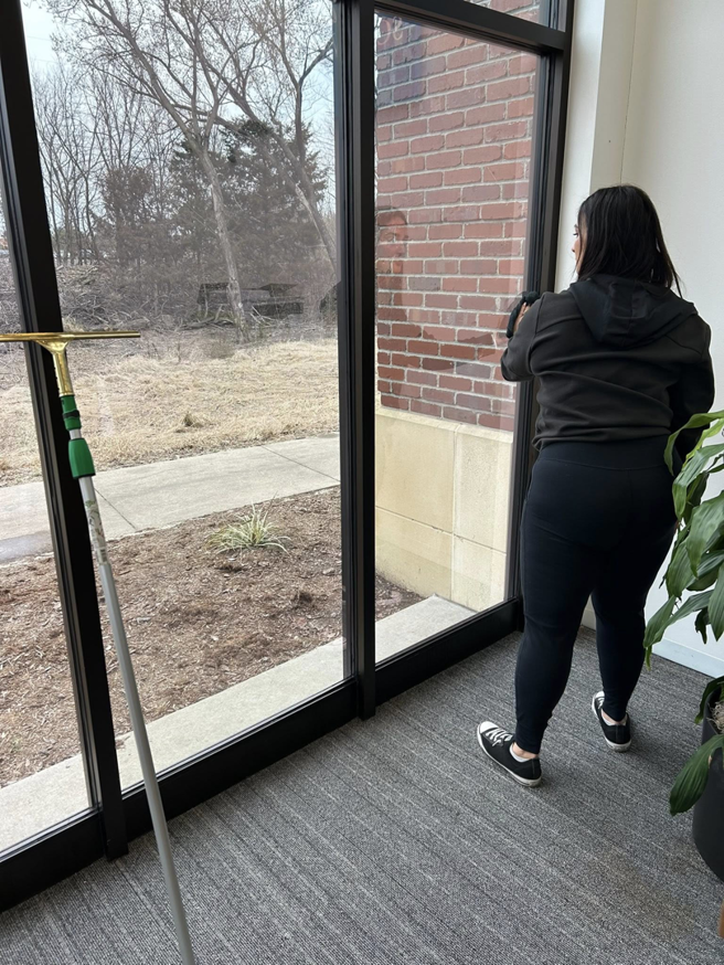A professional cleaner from Majestic Cleaning Services in Denver, CO, meticulously cleaning a large window with a squeegee.