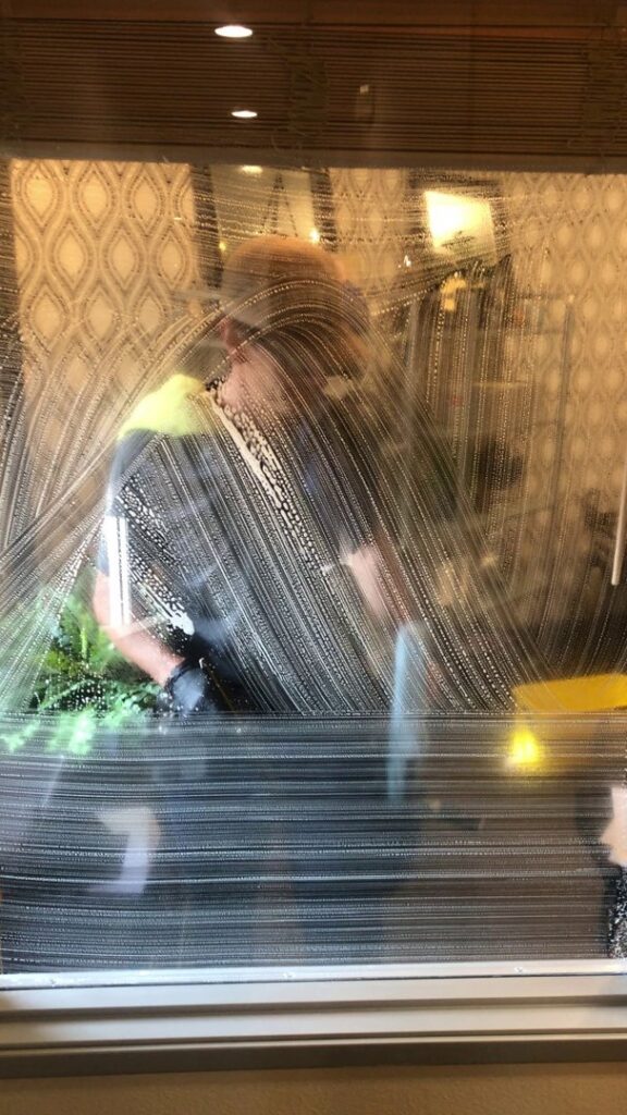 A professional performing window cleaning service, seen through a soapy window, by Idaho Gem Cleaning in Caldwell, ID.