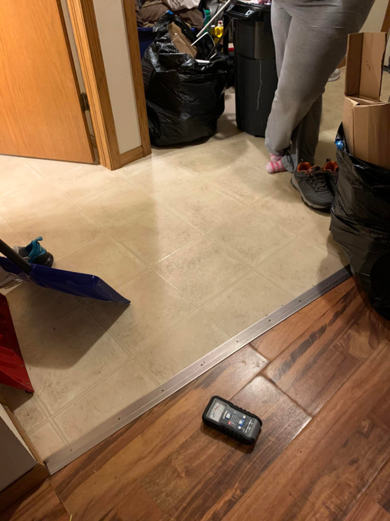A puddle of water on a concrete basement floor with a broom, indicating water damage in Janesville, WI by H&H2o Response & Restoration