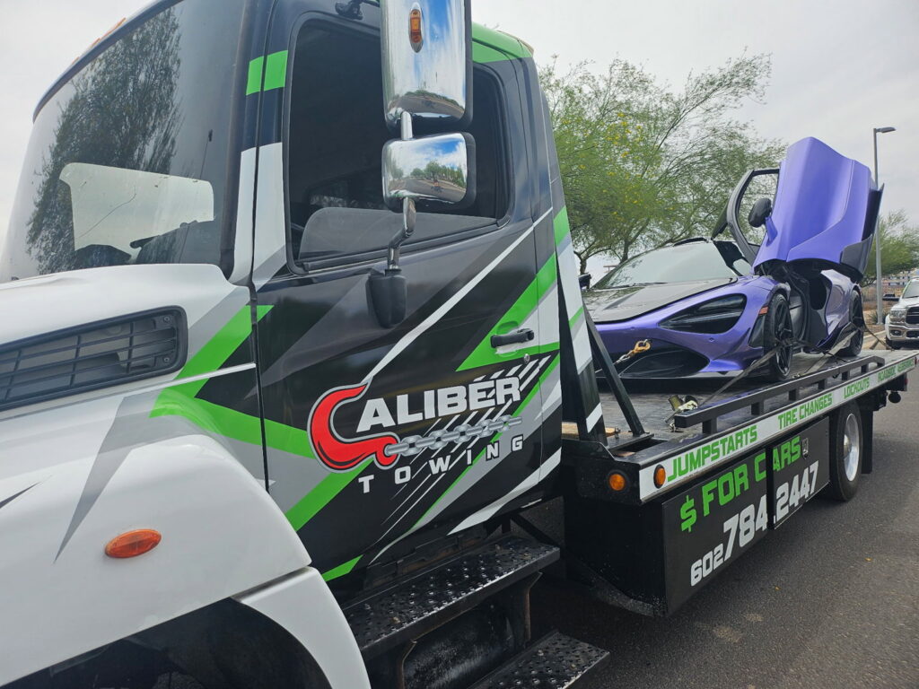 A purple McLaren sports car being transported on a flatbed tow truck by Caliber Towing in Phoenix, AZ.
