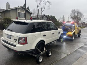A white Range Rover SUV is being towed by a wheel-lift tow truck from S&F Towing in Oakland, CA.