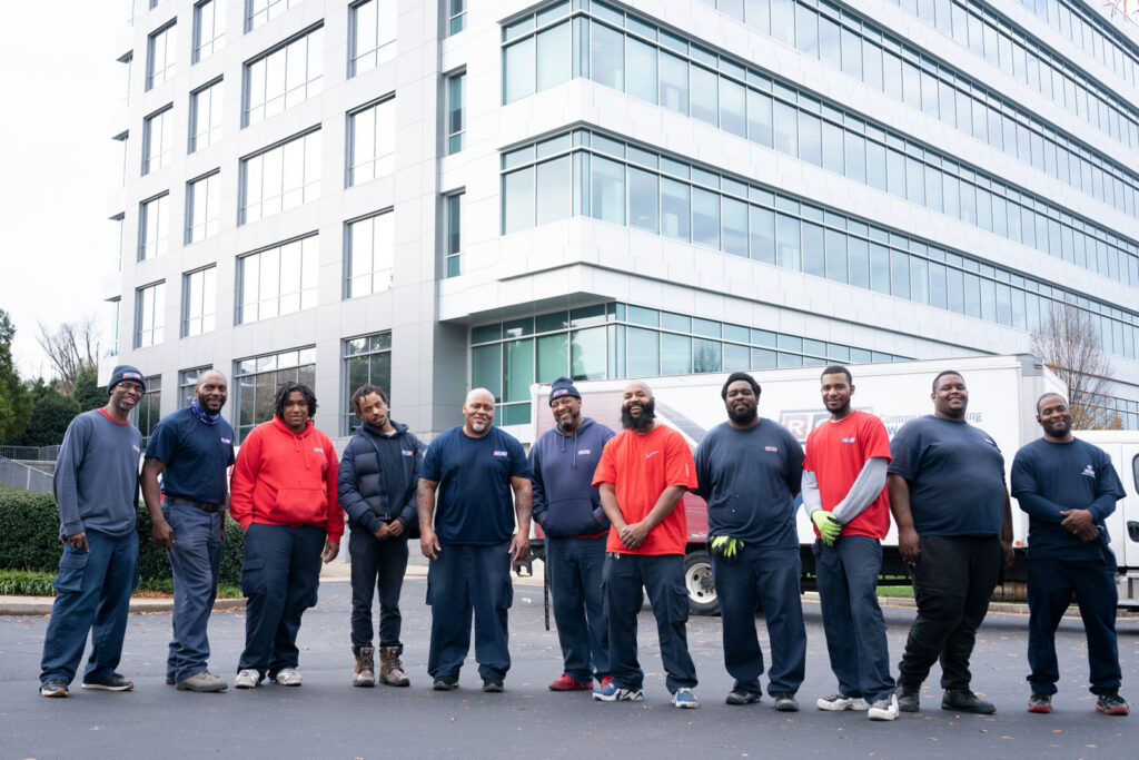 The professional moving team from RCS Moving & Storage stands proudly in front of an office building with their truck in Richmond, VA.