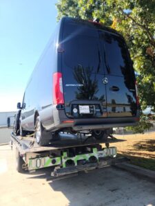 Rear view of a black Mercedes Sprinter van being towed on a flatbed truck by Pro-Tech Wrecker Service in Decatur, AL.