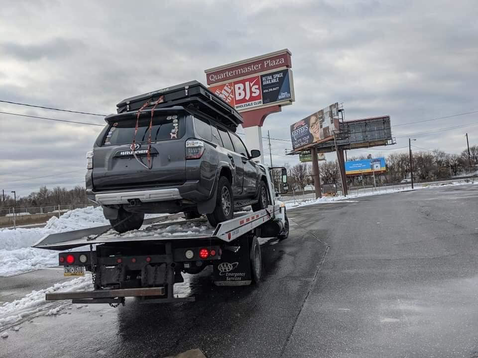 Rear view of a Kourouma Towing Services flatbed tow truck transporting an SUV near Quartermaster Plaza in Philadelphia, PA.