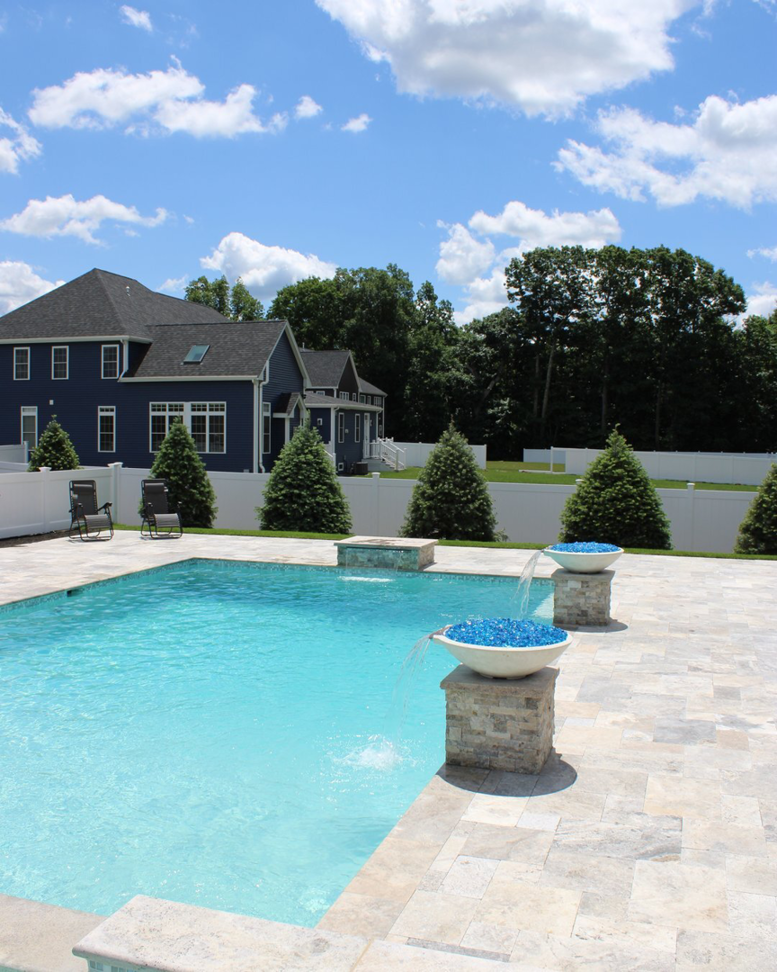A beautiful rectangular inground pool with decorative fire bowls and a spacious patio by Christman Pool Service in Portland, ME.