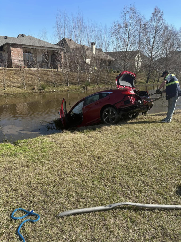 A red car being recovered from the water by a tow truck operator from Rick's Towing and Recovery in Lafayette, LA.