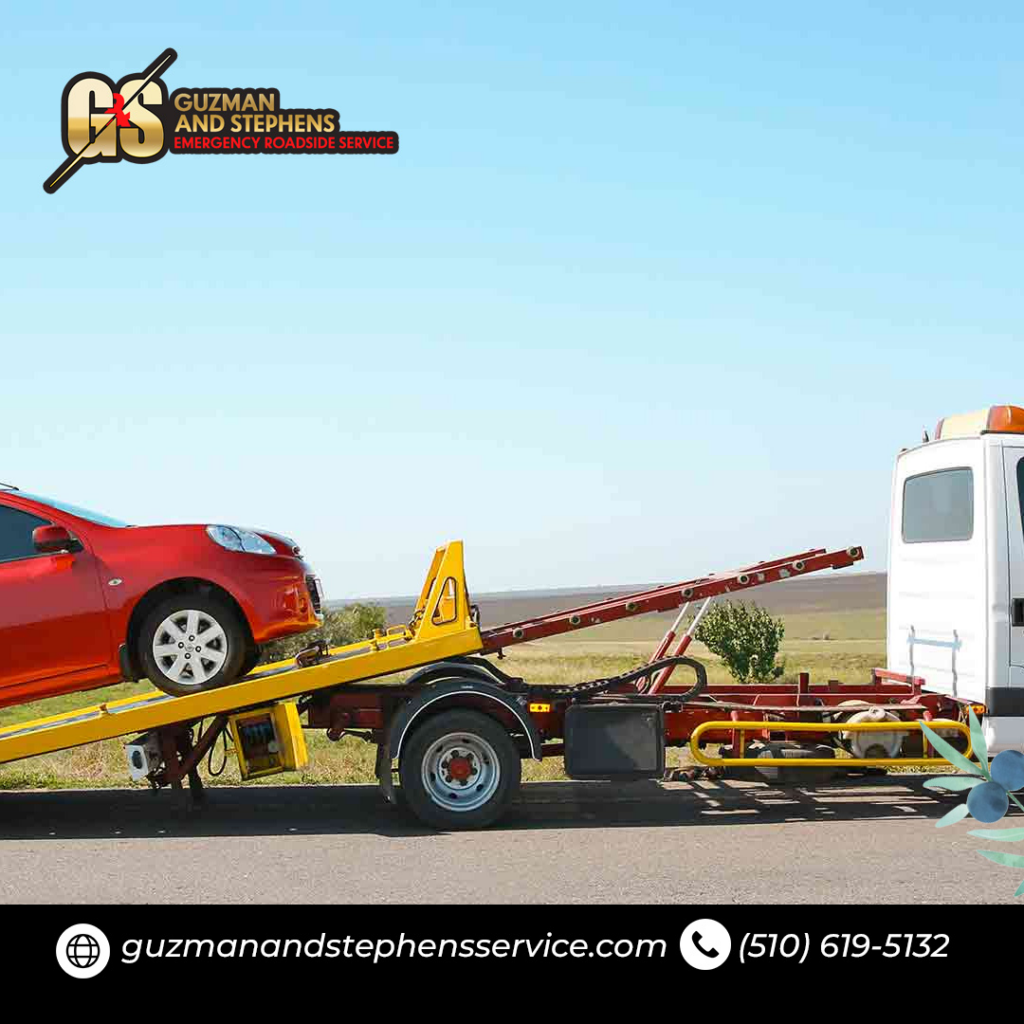 A red car being lifted by a wheel-lift tow truck for transport by Guzman Towing Services in Oakland, CA.